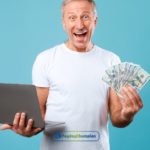 a person holding a dollar bill & a Laptop in their hand.