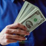 A man in a blue shirt holding a stack of money from installment loans online in Michigan