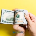 a person holding a dollar bill in their hand.