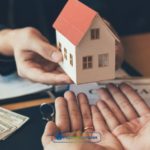 A person holding a house model over a pile of money obtained from a lease buyout loan