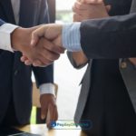 Two men shaking hands in front of a laptop after agreeing on a trade credit plan for their business
