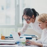 Two women working at a desk in an office reading about payday loans Austin