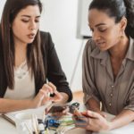 Two women sitting at a table looking at a cell phone searching for payday loans Charlotte