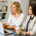 Two women sitting at a table looking at a laptop reading about payday loans in Seattle