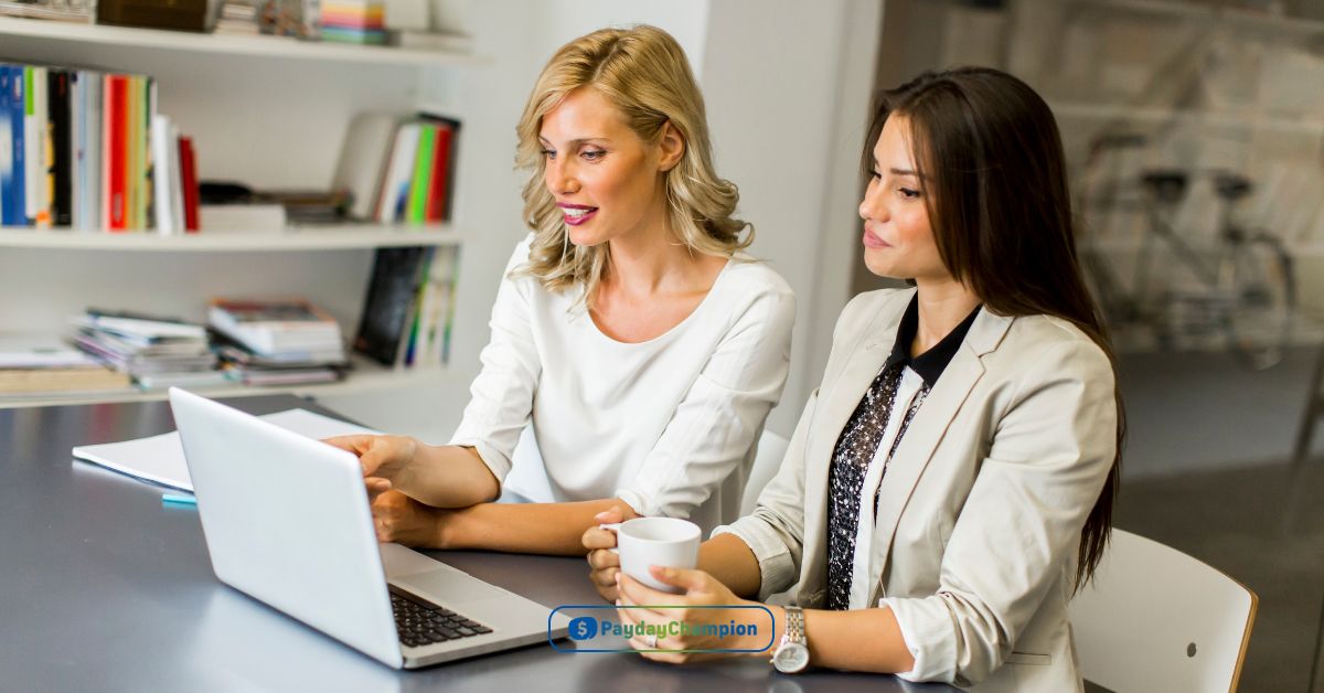 Two women sitting at a table looking at a laptop reading about payday loans in Seattle