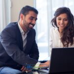 a man and a woman sitting on a couch looking at a laptop